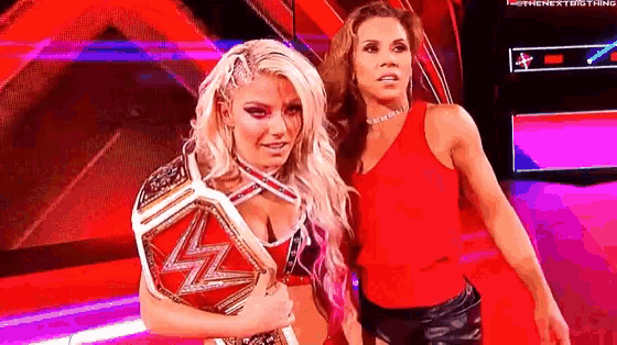 a couple of women standing next to each other on a stage . one of the women is holding a wrestling championship belt .