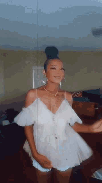 a woman in a white dress is standing in a living room and smiling .