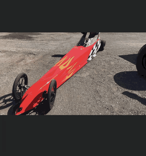 a red dragster with flames painted on the side is parked on a gravel road