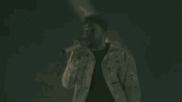a man is singing into a microphone in front of flames coming out of his mouth .