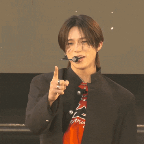 a young man wearing a black jacket and a red shirt with the letter a on it is pointing