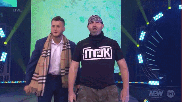 two men standing on a stage with one wearing a black shirt that says aew on it