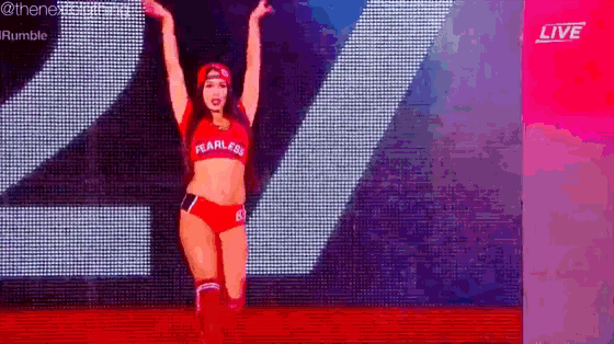 a woman is standing on a stage with her arms in the air and wearing a red outfit .