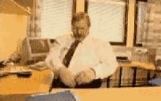 a man in a white shirt and tie sits at a desk in front of a computer