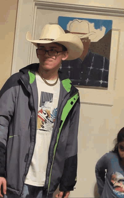 a young man wearing a cowboy hat and glasses is standing in front of a painting