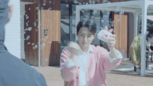 a man in a pink jacket is blowing soap bubbles at another man .