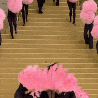a group of people are walking up a set of stairs with pink feathers on their heads