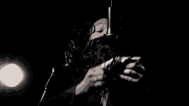 a man with a beard is singing into a microphone while holding a gun .