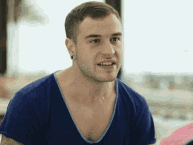 a man wearing a blue shirt and ear piercings looks at the camera