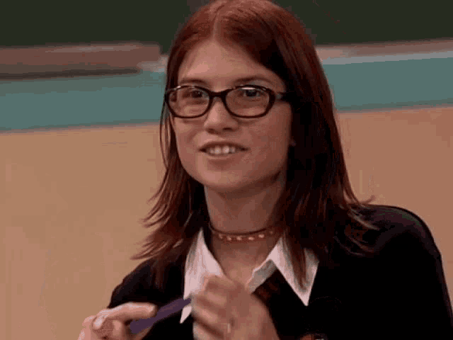 a woman with red hair wearing glasses and a choker is clapping her hands .