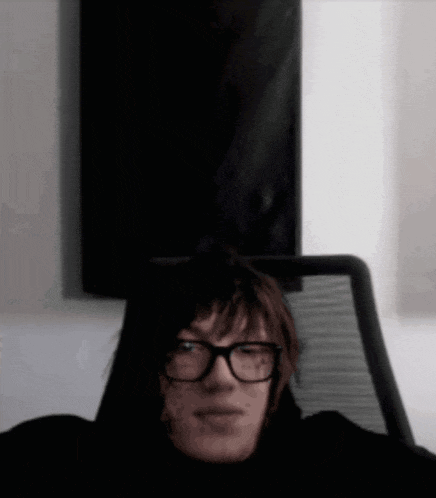 a man wearing glasses is sitting in a chair and looking at the camera