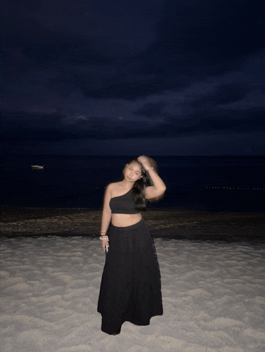 a woman in a black dress stands on a sandy beach at night