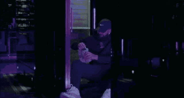 a man wearing a hat and a hoodie is sitting in front of a purple light .