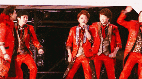 a group of men in red suits are standing on a stage with one man holding a microphone