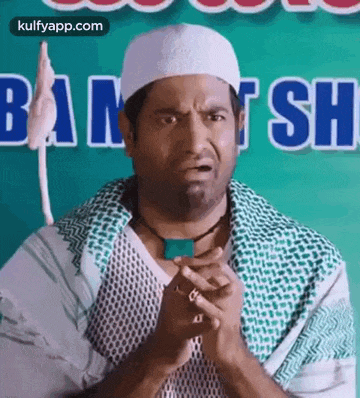 a man wearing a white hat and a green scarf is making a funny face with his hands folded .