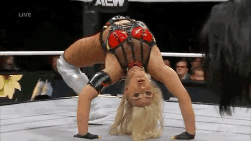 a woman is doing a handstand in a wrestling ring while a man watches .