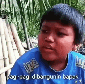 a young boy wearing a blue shirt with the words pagi-pagi dibangunin bapak on it .
