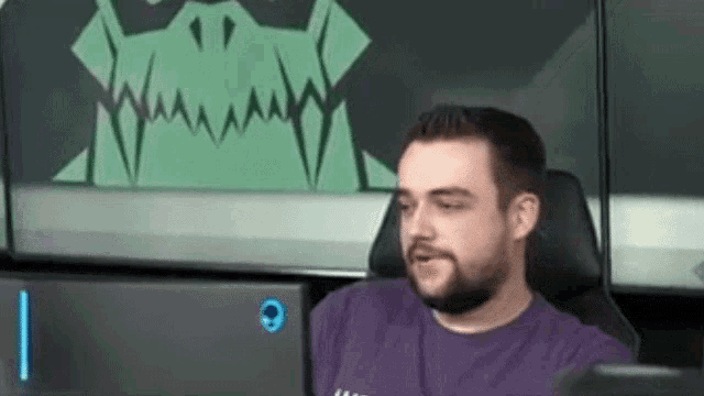 a man in a purple shirt is sitting in front of a computer screen with a green monster on it .