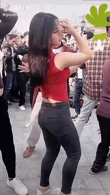 a woman in a red top and gray jeans is dancing in front of a crowd of people .