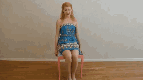 a woman is sitting on a pink chair with a blue dress on