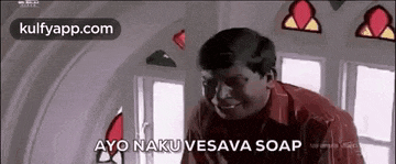 a man in a red shirt is standing in front of a window and saying `` ayo naku vesama soap '' .