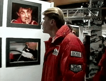 a man in a red jacket with the word boss on the sleeve is looking at pictures on a wall .