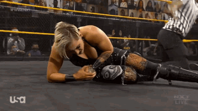 a woman is laying on the ground in a wrestling ring while a referee looks on ..