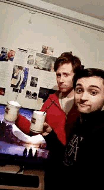 two men standing next to each other holding mugs in front of a monitor
