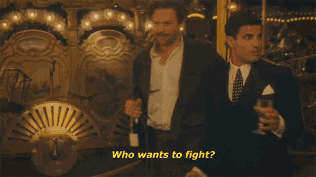 two men are standing next to each other and one of them says who wants to fight .