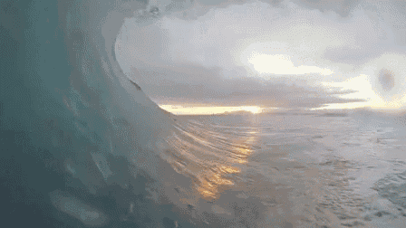 a wave is breaking on the beach and the sun is reflected in the water