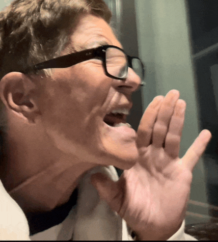 a man wearing glasses is shouting with his hand