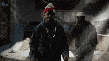 a man in a santa hat stands next to another man in a black jacket