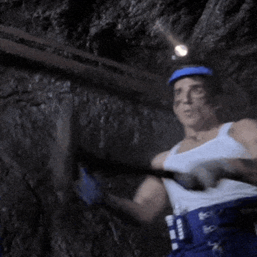 a man wearing a white tank top and a blue helmet holds a hammer