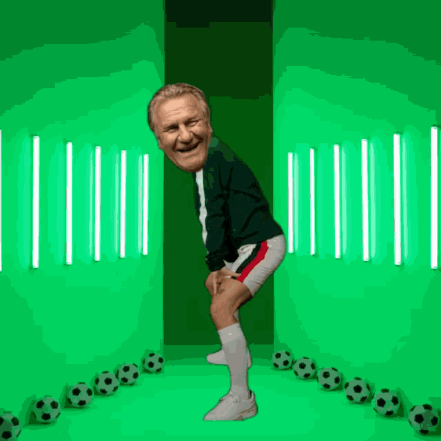a man is standing in front of a green wall with soccer balls