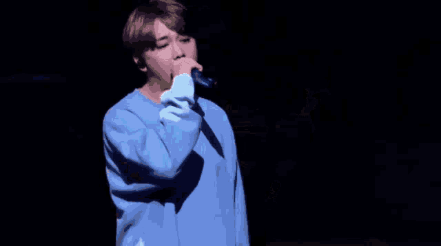 a young man wearing a blue sweater is standing on a stage in front of a black background .
