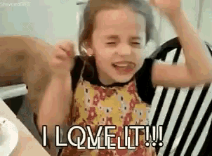 a little girl is sitting in a chair with her hands in the air and says `` i love it '' .