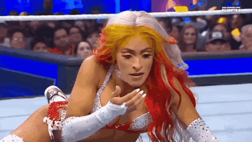 a female wrestler with red and white hair is laying on the ground in a wrestling ring .