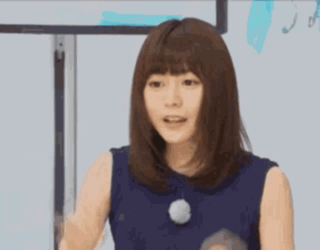 a woman in a blue dress is standing in front of a white board and making a fist .