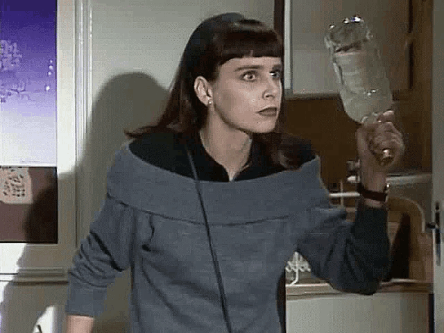 a woman in a blue sweater is holding a glass of wine in her hand .