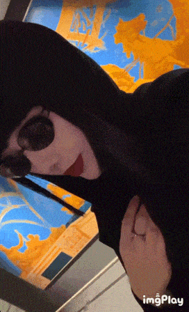 a person wearing a black hoodie and sunglasses is standing in front of a painting ..
