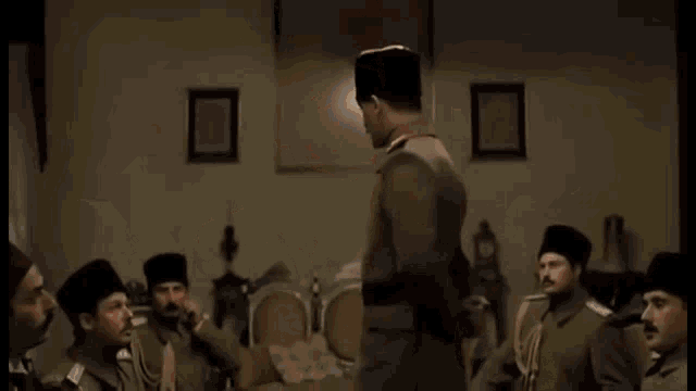 a group of men in military uniforms are sitting in a room with a man standing in the middle