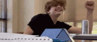 a boy sitting at a desk with his fist up