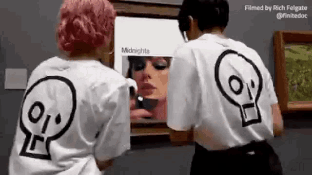 two people are standing next to each other in front of a painting .