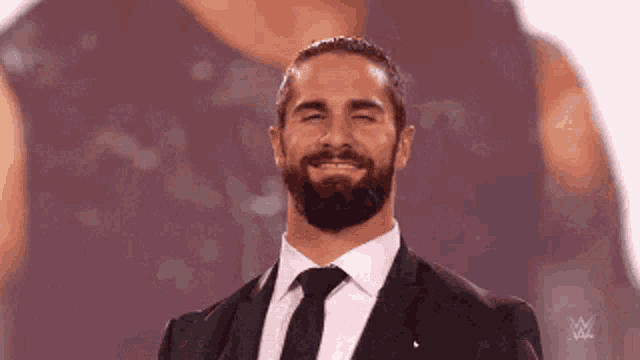 a man with a beard wearing a suit and tie is smiling with his eyes closed .