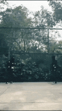 a couple of people standing on a basketball court in front of a fence .