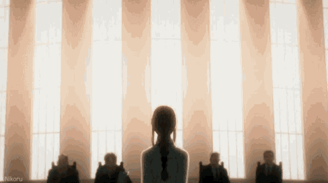 a woman is standing in front of a group of people sitting in chairs in a room with a lot of windows .