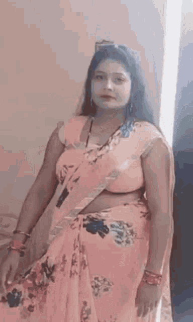 a woman in a pink floral saree is posing for a picture .