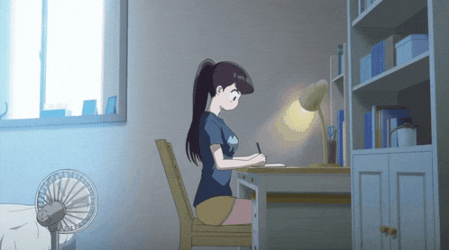 a girl is sitting at a desk with a fan in the foreground