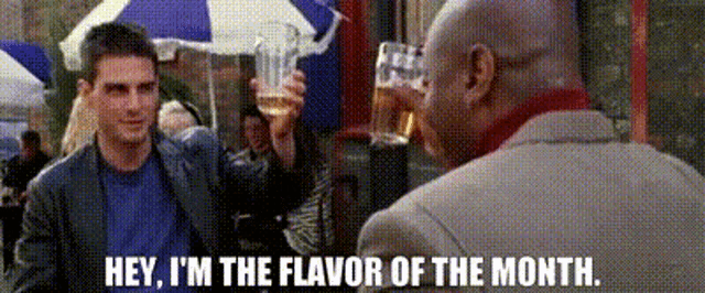 a man in a suit is talking to another man while holding a glass of beer .