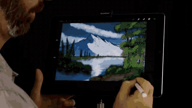 a person is drawing a picture of a mountain and a lake on a tablet